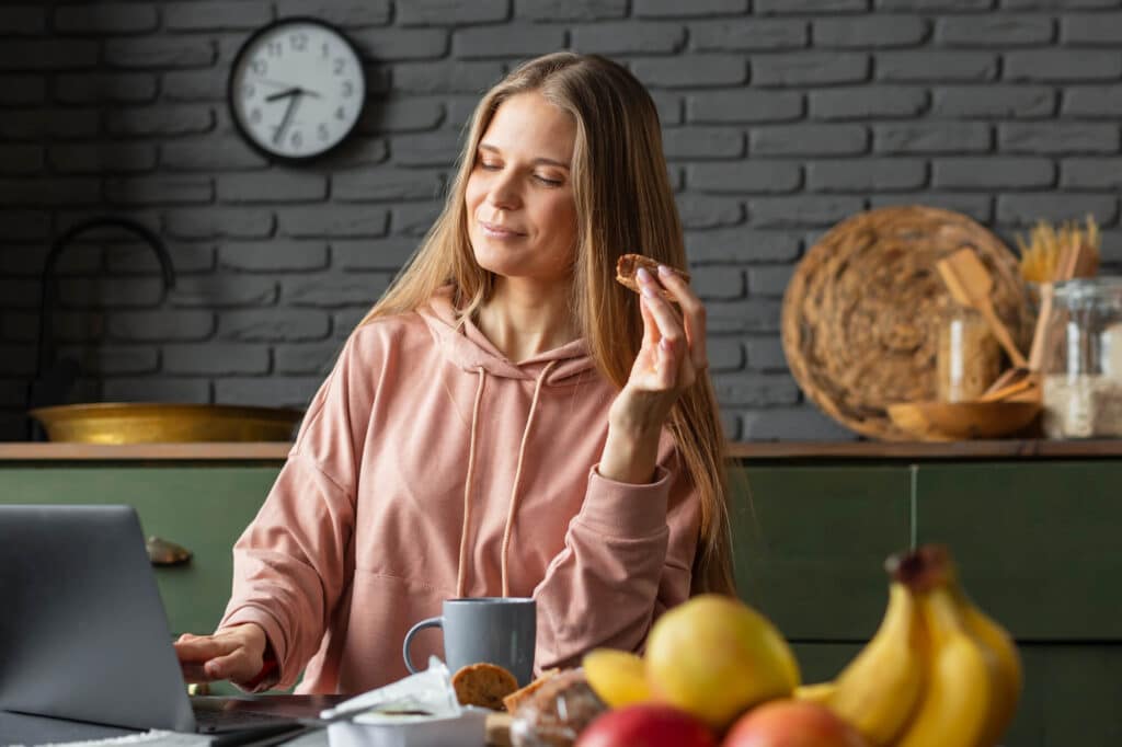Femme savourant une collation saine tout en travaillant dans sa cuisine