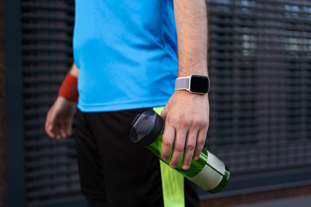 Sportif tenant une gourde verte et portant une montre connectée