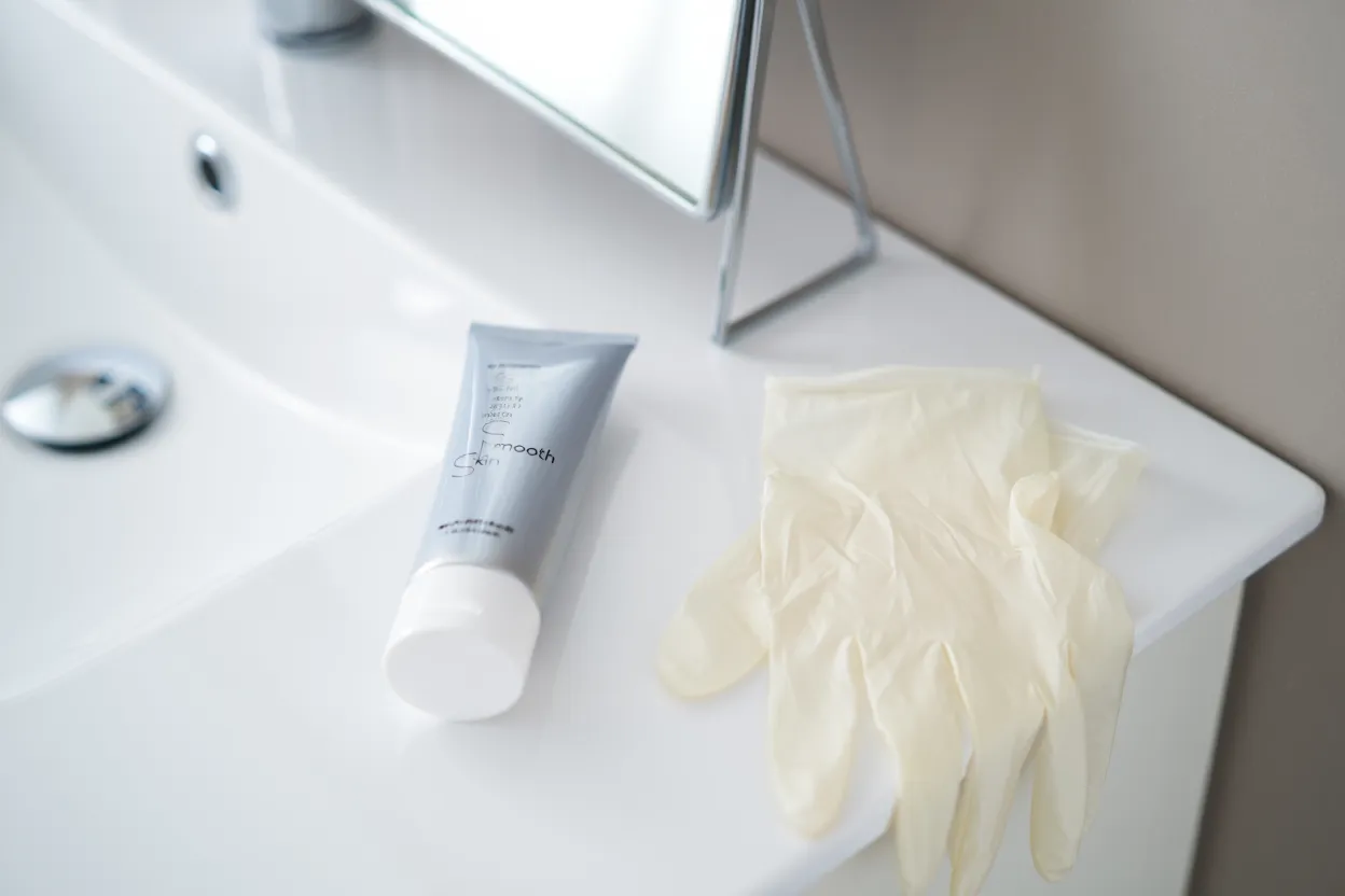 Crème et gants en latex sur lavabo.